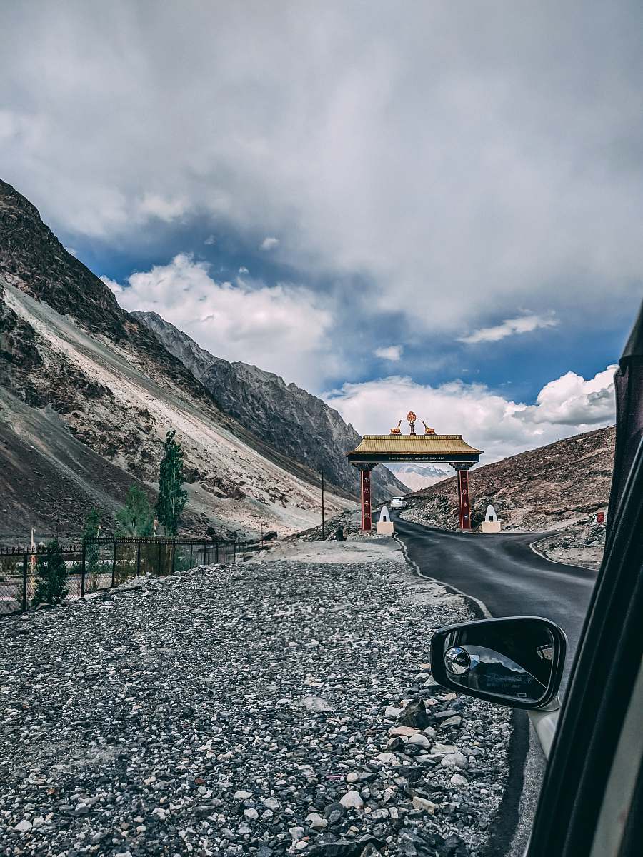dirt road red and brown historic gate viewing mountain under white and blue sky gravel